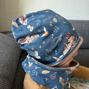 Może przedstawiać: Niebieski zestaw czapki i komina z nadrukiem w stylu Harry'ego Pottera. Nadruk przedstawia zamek Hogwart, sowy, znicz i liczbę "9 3/4".