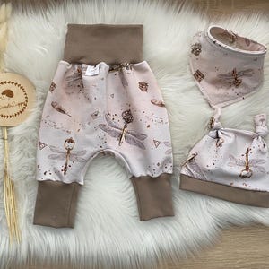 Puede incluir: Un conjunto de ropa para bebé con estampado de libélula y llave. El conjunto incluye un pantalón, un gorro y un babero. El pantalón es marrón y blanco con una cintura marrón. El gorro es marrón y blanco con un borde marrón. El babero es marrón y blanco con un borde marrón.