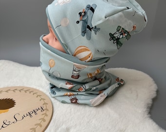 May include: A light blue knit hat and matching neck warmer with a whimsical pattern of hot air balloons, airplanes, and woodland animals.