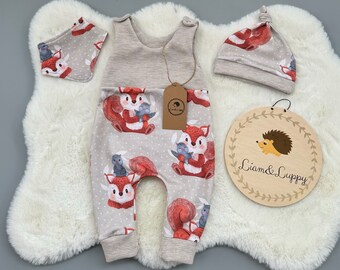 Op de afbeelding: Een baby-outfitset met een grijs-wit gestreepte romper, een grijs-witte slabbetje en een grijs-witte muts. De romper heeft een eekhoornprint met rode, bruine en blauwe accenten. De slabbetje en de muts hebben ook een eekhoornprint. De set is gemarkeerd met "Liam & Luppy".