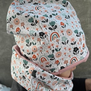 Peut inclure: Un ensemble bonnet et tour de cou blanc avec un motif floral et arc-en-ciel. Le tissu est doux et confortable.