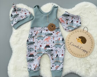 Op de afbeelding: Een baby-outfitset bestaande uit een blauwe wafel gebreide romper met een dinosaurusprint, een bijpassende blauwe wafel gebreide muts met een geknoopte bovenkant en een blauwe slab met een dinosaurusprint. De set ligt op een wit pluche oppervlak met een houten bord waarop "Liam & Luppy" staat.