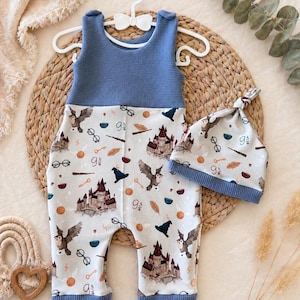Könnte beinhalten: Baby-Outfit-Set mit blauem Oberteil und gemusterter Hose, mit Eulen, Burgen und magischen Symbolen. Ein passender Hut ist enthalten. Das Set wird auf einem weißen Kleiderbügel präsentiert. Maße in Zentimetern.
