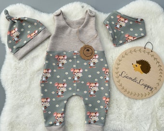 May include: A baby outfit set with a green and brown jumpsuit with a bear print, a matching hat, and a face mask. The jumpsuit has a brown and white striped waistband and leg cuffs. The set is on a white fluffy surface with a wooden sign that says "Liam & Luppy".