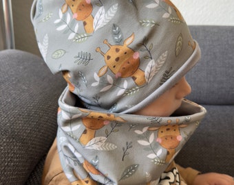 May include: A grey knitted hat and matching neck warmer with a pattern of giraffes and leaves.
