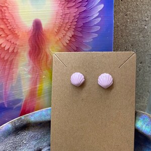 May include: A pair of pink seashell stud earrings displayed on a brown card.