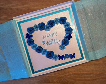 May include: A blue and white card with a heart-shaped design made of paper flowers and butterflies. The card says "Happy Birthday".