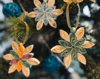 May include: Five paper quilled snowflake ornaments in various colors, including green, blue, and pink, hanging on a Christmas tree.