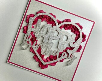 May include: A silver glitter card with a pink paper flower heart that says "Happy Birthday" in silver glitter.