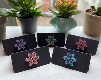 May include: Five black cards with a decorative paper flower on each. The flowers are purple, pink, blue, green, and light blue.