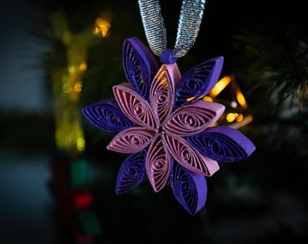 May include: A purple and pink paper snowflake ornament with glitter, hanging from a silver ribbon.