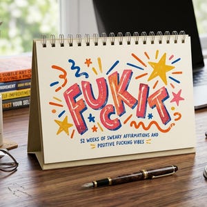 May include: A spiral-bound desk calendar with a cream-coloured cover featuring the text FUK IT in large, colourful, hand-drawn style letters, surrounded by stars and squiggles, with the subtitle 52 WEEKS OF SWEARY AFFIRMATIONS AND POSITIVE FUCKING VIBES.