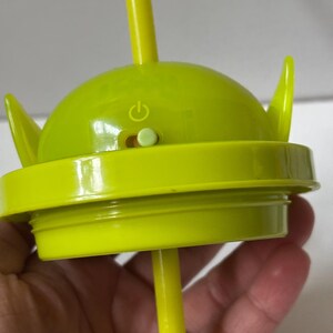以下が含まれることがあります： ライムグリーンのエイリアンをテーマにしたカップの蓋と、お揃いのストロー。 蓋には、2つの尖った耳と電源ボタンが付いた丸みを帯びた上部があります。 ストローは蓋の中央から差し込まれています。