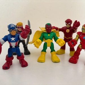 May include: A collection of colorful superhero action figures, including Captain America with his shield, Hawkeye with a bow, Vision, The Flash, and Iron Man. The figures are in various poses, showcasing their iconic costumes.