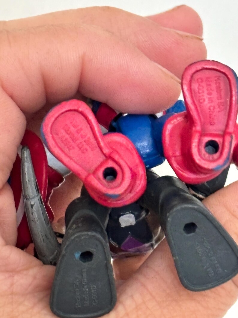 May include: A close-up of several small action figure feet and legs. The figures are primarily black, red, and blue. The feet have holes in the soles. The figures are held in a hand.