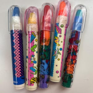 May include: Five multi-colored markers with clear plastic caps. Each marker features a unique barrel design, including patterns of fish, sea creatures, and scales. The markers have vibrant ink tips in blue, yellow, red, orange, and teal colors.