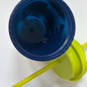 以下が含まれることがあります： 青いタンブラーと、お揃いの蓋と黄色のストロー。タンブラーの内側は濃い青色で、蓋は明るい緑色です。ストローは鮮やかな黄色で、カラフルなコントラストを生み出しています。タンブラーは冷たい飲み物用に設計されています。