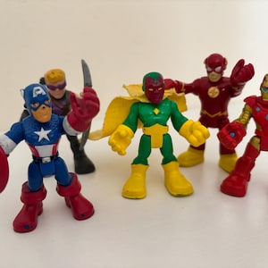 May include: A collection of colorful superhero action figures, including Captain America with his shield, Iron Man, The Flash, and Vision. The figures are in various poses, with vibrant red, blue, and yellow colors.