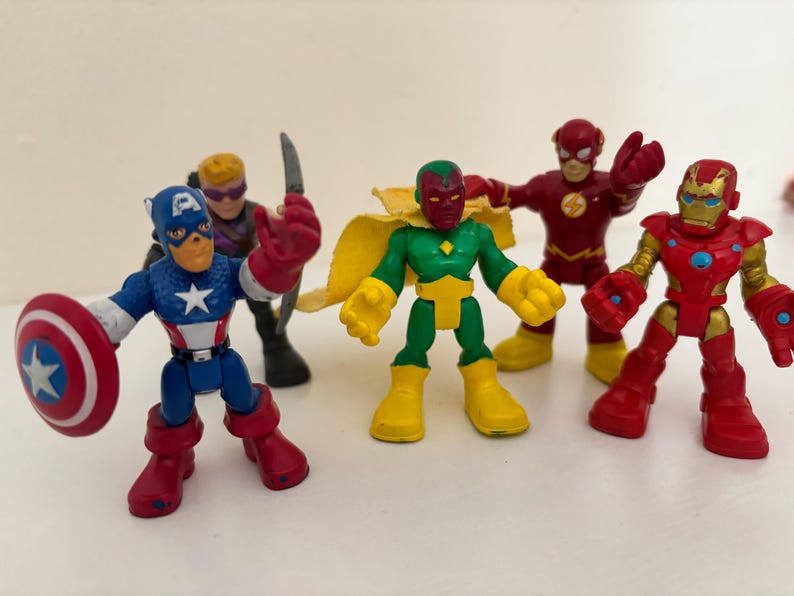 May include: A collection of colorful superhero action figures, including Captain America with his shield, Iron Man, The Flash, and Vision. The figures are in various poses, with vibrant red, blue, and yellow colors.