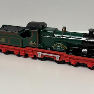May include: A die-cast model steam locomotive painted in dark green with a black roof and smokebox. The train features a bright red chassis, gold lettering reading City of Truro, and the number 3440 on the side. It includes a coal tender.