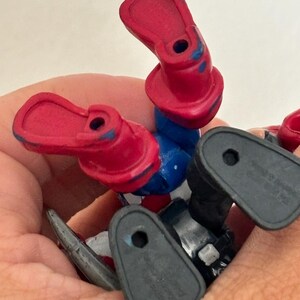 May include: A close-up of a toy action figure's legs and feet. The figure has red boots, blue pants, and black feet. The figure is lying on its back, with the feet pointing upwards.