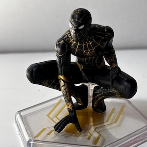 Puede incluir: Figura de Spider-Man negro y dorado en cuclillas. La figura tiene intrincados detalles dorados en el traje y est&aacute; montada sobre una base hexagonal transparente con detalles dorados. Es un art&iacute;culo de colecci&oacute;n.