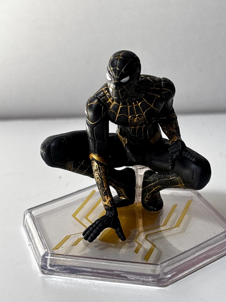 Puede incluir: Figura de Spider-Man negro y dorado en cuclillas. La figura tiene intrincados detalles dorados en el traje y est&aacute; montada sobre una base hexagonal transparente con detalles dorados. Es un art&iacute;culo de colecci&oacute;n.