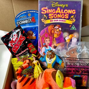 May include: A box filled with Disney-themed items. Includes a VHS tape of "Disney's Sing Along Songs: Be Our Guest", a "Connect 4" game, a plush tiger, candy, and figurines of Belle and the Beast from "Beauty and the Beast".