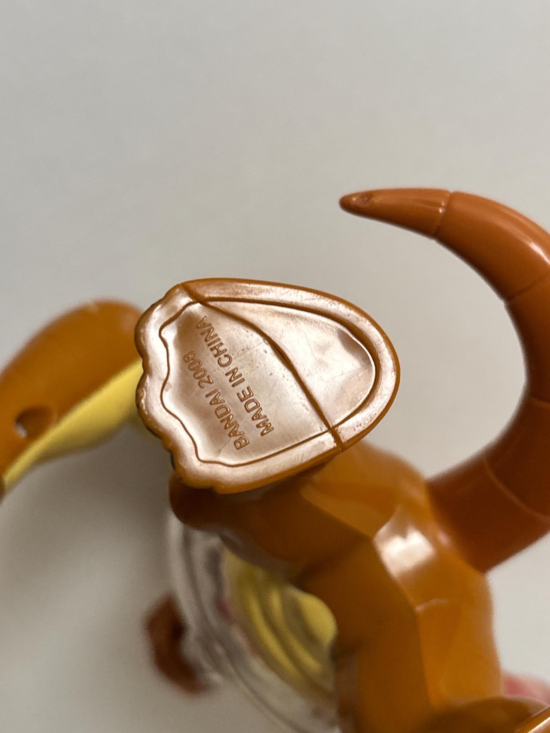 May include: A brown plastic toy figure with a curved tail and a yellow section. The underside of the figure has the text "BANDAI 2008 MADE IN CHINA". The toy is made of shiny plastic.