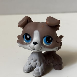 May include: A small, plastic toy dog with brown and white fur. The dog has large blue eyes and a friendly expression. The toy is a collectible item, likely part of a larger set of animal figures.