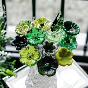 May include: A glass vase filled with a bouquet of green and yellow glass flowers. The flowers are shaped like simple blossoms with rounded petals.