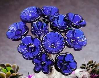 Peut inclure: Un bouquet de fleurs en verre bleu dans un vase en verre transparent. Les fleurs sont disposées en grappe et ont un aspect délicat et fantaisiste. Le vase est transparent et a une surface texturée.