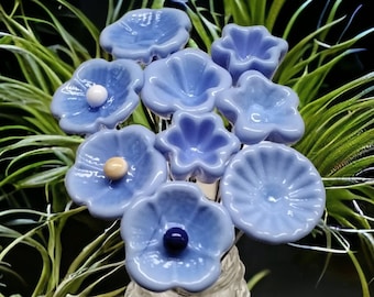May include: A bouquet of blue glass flowers with white and yellow centres in a clear glass vase. The flowers are arranged in a cluster and have a delicate, whimsical appearance.
