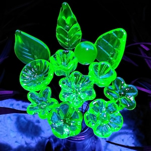 May include: A bouquet of green glass flowers in a vase. The flowers are made of uranium glass and glow under a black light.
