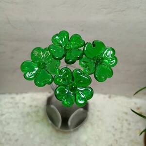 May include: Four green glass shamrock flowers in a vase. The flowers are made of glass and have a shiny finish.