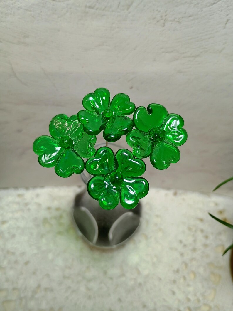 May include: Four green glass shamrock flowers in a vase. The flowers are made of glass and have a shiny finish.