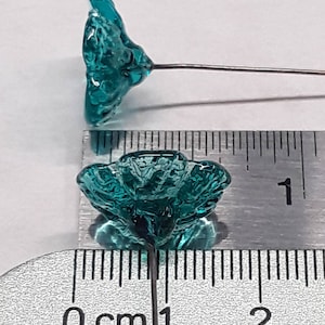 May include: Teal blue glass flower with a wire stem. The flower is approximately 1 cm in diameter.