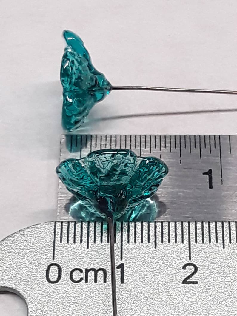 May include: Teal blue glass flower with a wire stem. The flower is approximately 1 cm in diameter.