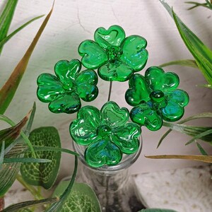 May include: Four green glass shamrock flowers on wire stems in a clear glass vase.