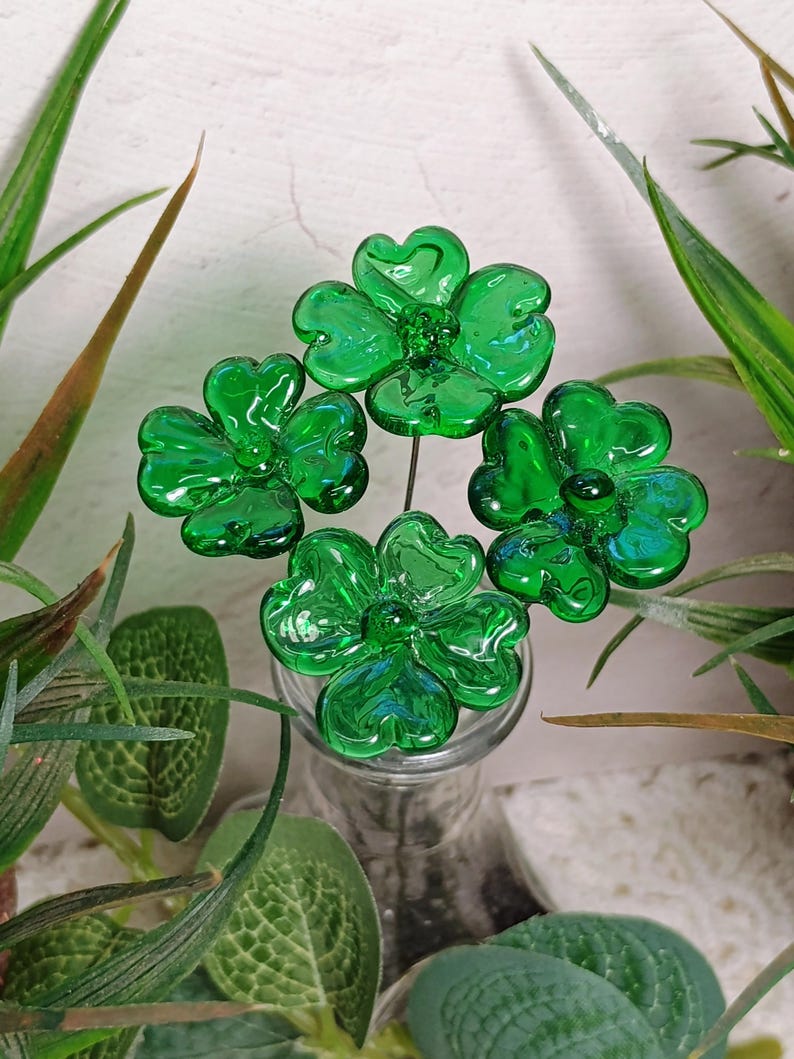 May include: Four green glass shamrock flowers on wire stems in a clear glass vase.