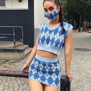 以下が含まれることがあります： 青と白のアーガイル柄のニットのクロップトップとスカートのセット。トップはVネックでノースリーブ。スカートはハイウエストのミニスカートです。