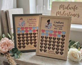 May include: Two wooden framed signs featuring a cartoon illustration of a person, the name Lindsey, Bournemouth University 2026-2029, and the text Midwife in the making, with rows of pink and blue heart cutouts for tracking progress.
