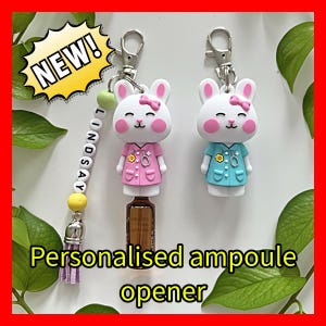 May include: Two novelty ampoule openers with a white bunny design, pink cheeks, and a bow, dressed in pink and blue medical uniforms. The openers are attached to keychains. The image includes the text "Personalised ampoule opener" and "NEW!"