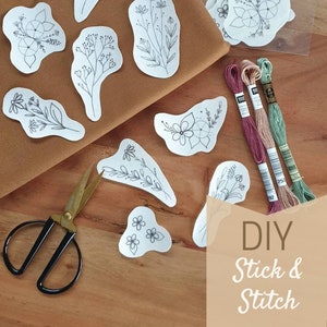 以下が含まれることがあります： 花柄のデザインで、自分で貼って刺繍できるDIYキット。キットには、花柄のデザインが印刷されたシート、3色の刺繍糸、小さなハサミが1つ入っています。