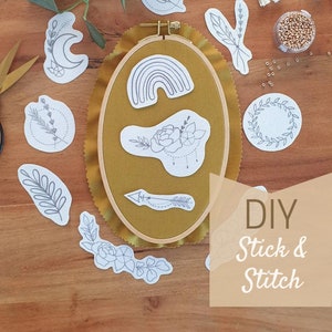 Könnte beinhalten: Ein Set mit DIY-Stickmustern mit verschiedenen Designs, darunter ein Halbmond, ein Regenbogen, eine Blume, ein Pfeil und Blätter. Die Muster sind auf weißem Papier gedruckt und bereit zum Sticken auf Stoff. Das Bild zeigt auch einen Stickrahmen, Stickgarn und Perlen.
