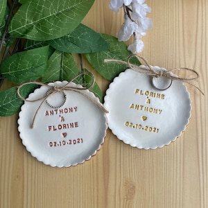 Peut inclure: Deux coupelles à anneaux en céramique blanche avec inscription dorée. La coupelle de gauche indique "Anthony à Florine" avec un cœur et la date "02.10.2021". La coupelle de droite indique "Florine à Anthony" avec un cœur et la date "02.10.2021".
