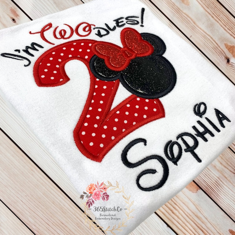 May include: A white onesie with red and white polka dot fabric. The onesie has a red number 2 with a black and red Minnie Mouse head on top. The text "I'm Twodles!" is embroidered above the number and the name "Sophia" is embroidered below the number.