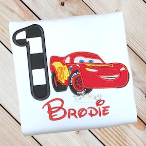 Pu&ograve; includere: Maglietta bianca con un'auto da corsa rossa dei cartoni animati, il numero 95 e il nome "Brodie" in rosso. Un numero 1 a scacchi in bianco e nero &egrave; a sinistra. Questa maglietta &egrave; probabilmente per un compleanno di bambini.