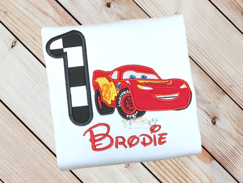 Pu&ograve; includere: Maglietta bianca con un'auto da corsa rossa dei cartoni animati, il numero 95 e il nome "Brodie" in rosso. Un numero 1 a scacchi in bianco e nero &egrave; a sinistra. Questa maglietta &egrave; probabilmente per un compleanno di bambini.