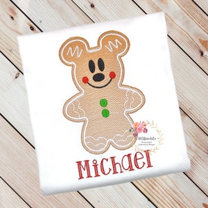May include: A gingerbread man with Mickey Mouse ears and a red smile, embroidered on a white shirt with the name "Michael" in red lettering.